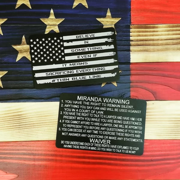 Black custom metal Miranda cards on a wooden flag background with American Flag and Sacrifice Quote