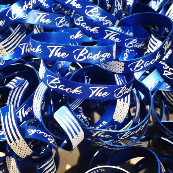 a pile of custom, blue memorial bracelets with a flag and "back the blue" engraved on it