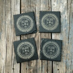 Four coasters laid on a wooden table with the SLED (South Carolina Law Enforcement Devision) logo